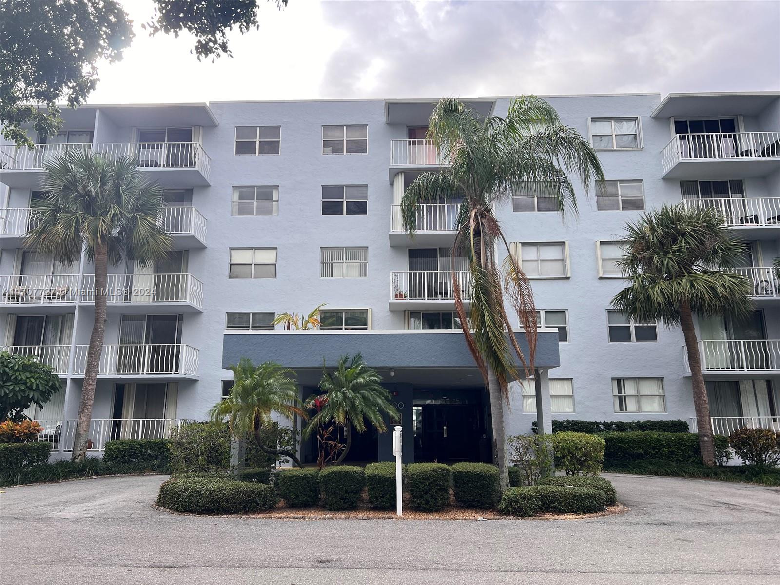 a front view of a multi story building with yard and parking space