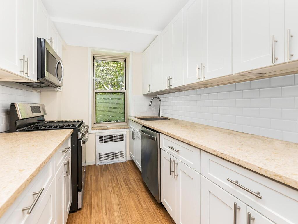 Kitchen featuring light stone countertops, light hardwood / wood-style floors, stainless steel appliances, sink, and white cabinets