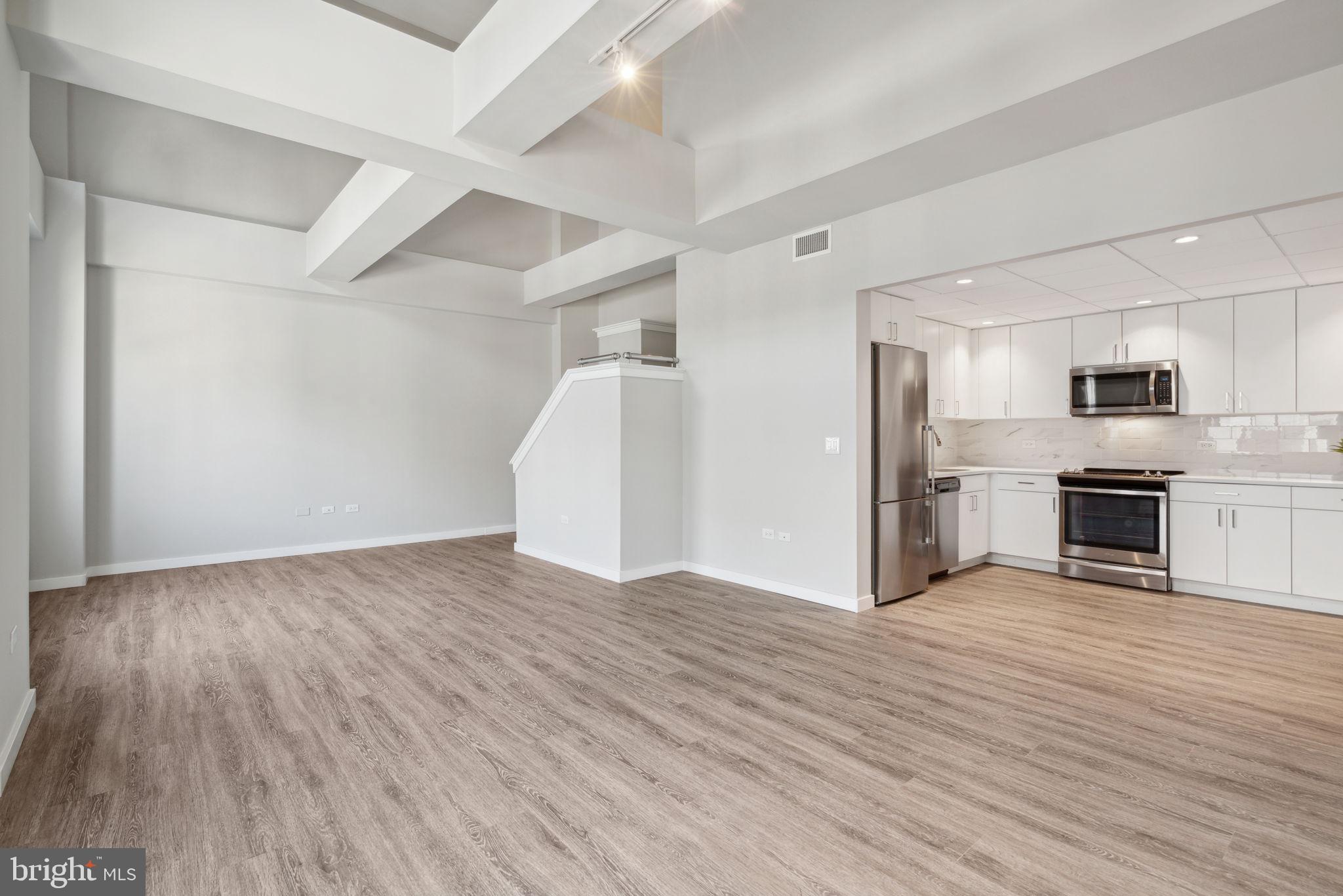 a view of an empty room with wooden floor and a kitchen