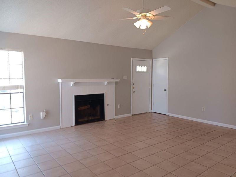 a view of an empty room with chandelier fan and fire place