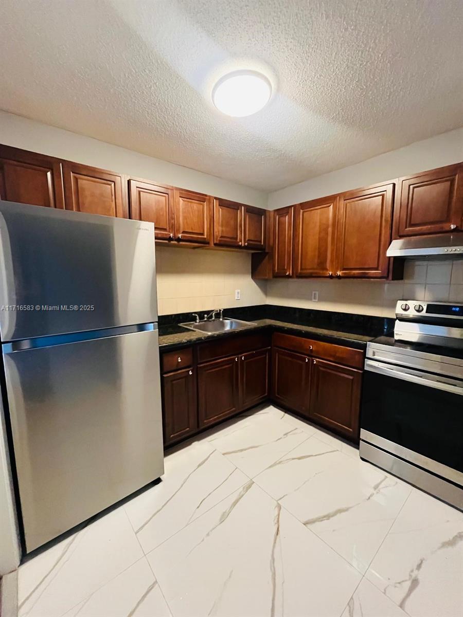 a kitchen with granite countertop a refrigerator and a stove top oven