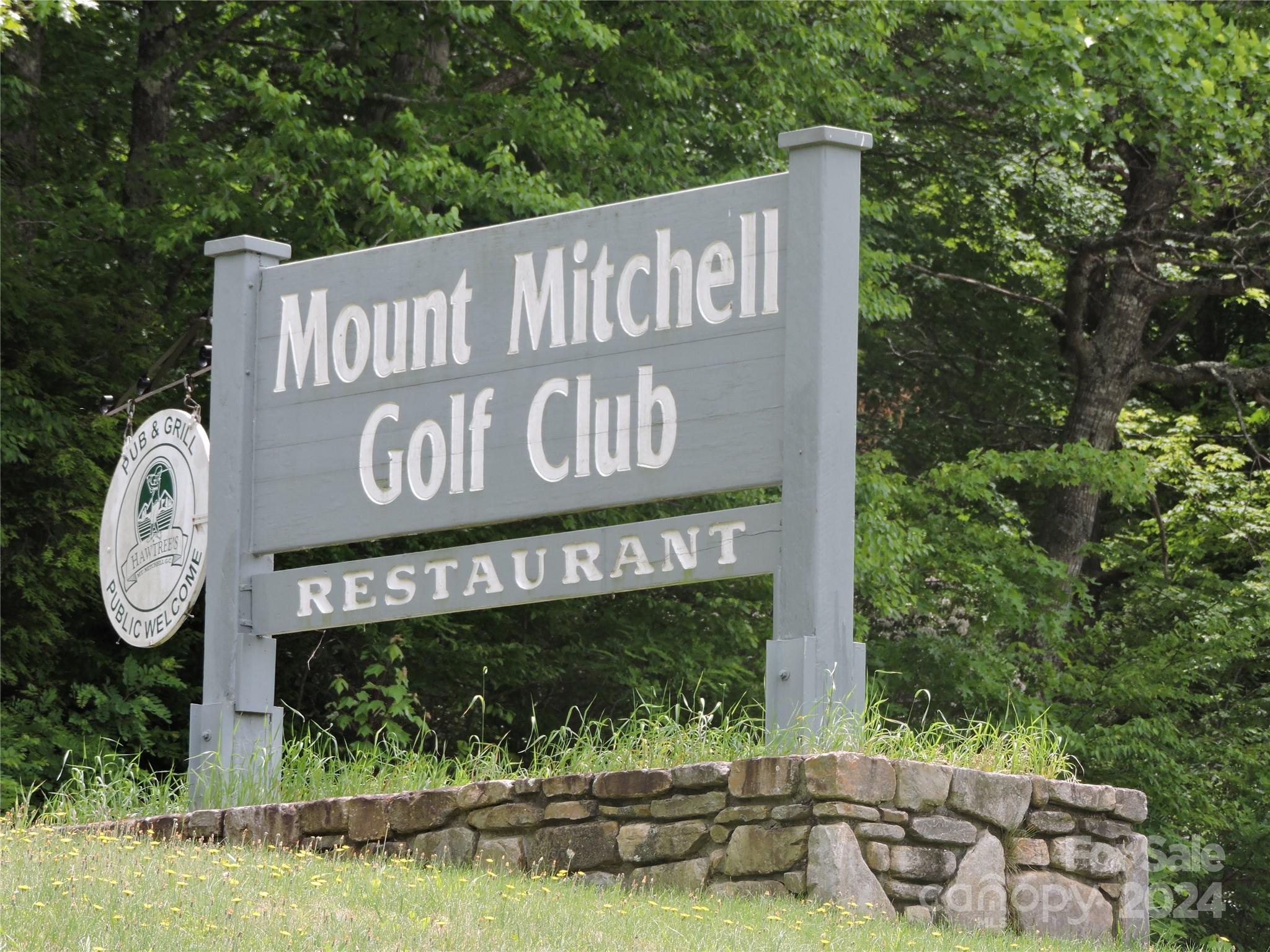 a view of sign board with yard and mountain view in the background