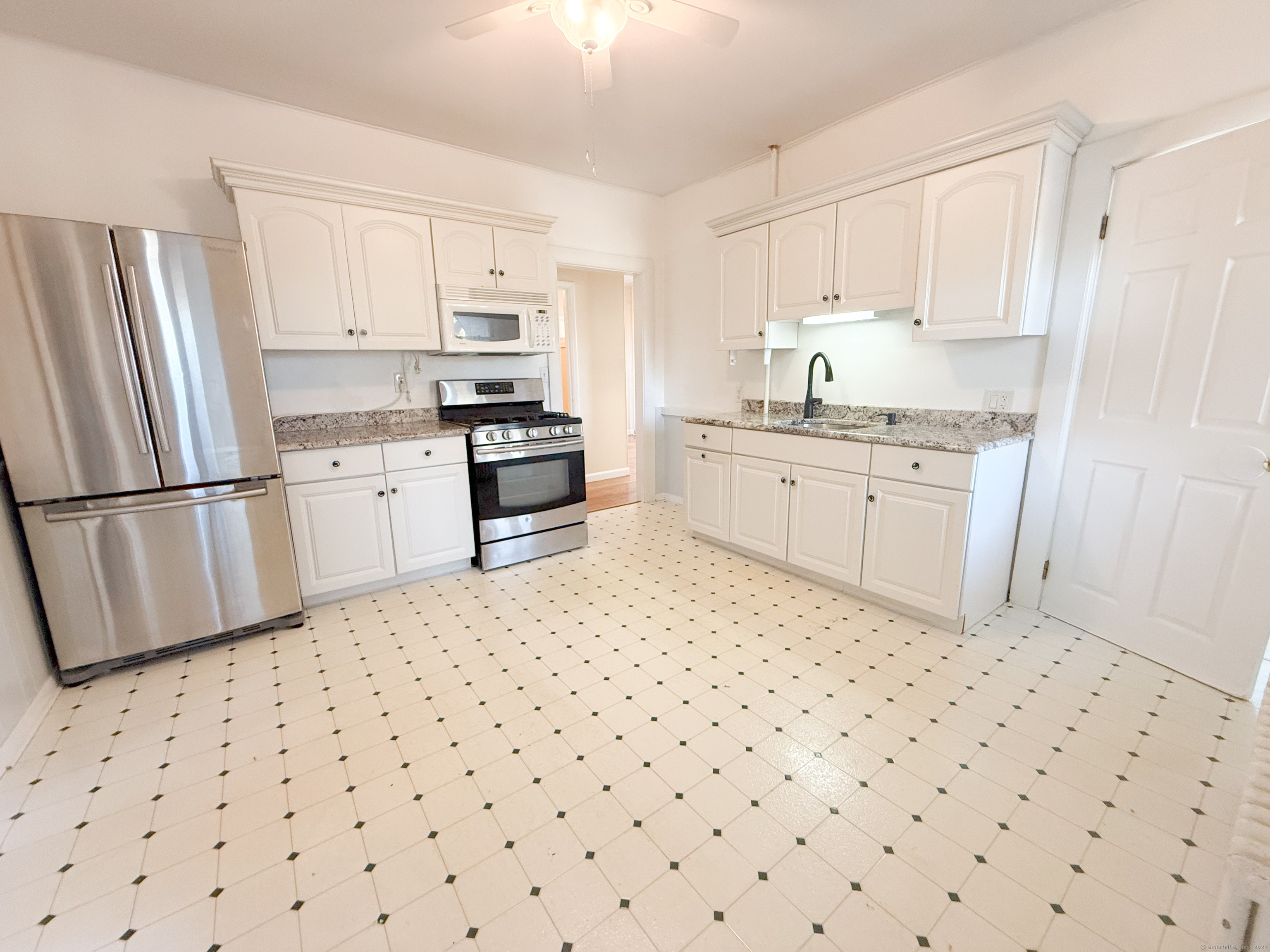 a kitchen with granite countertop a sink a stove a refrigerator and white cabinets