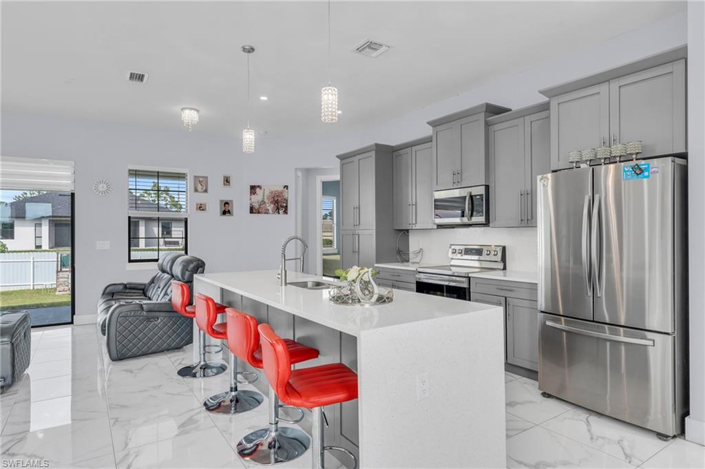 Kitchen with a kitchen island with sink, hanging light fixtures, sink, a kitchen bar, and appliances with stainless steel finishes