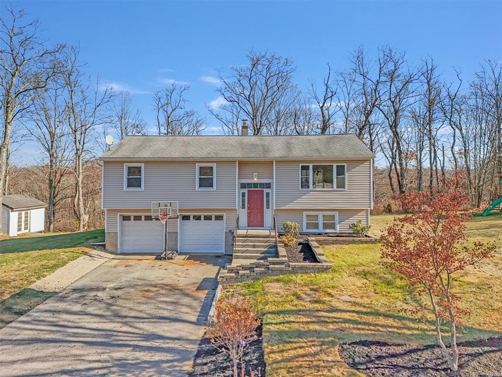 Bi-level home featuring stone like steps, a front manicured landscaped yard and a garage