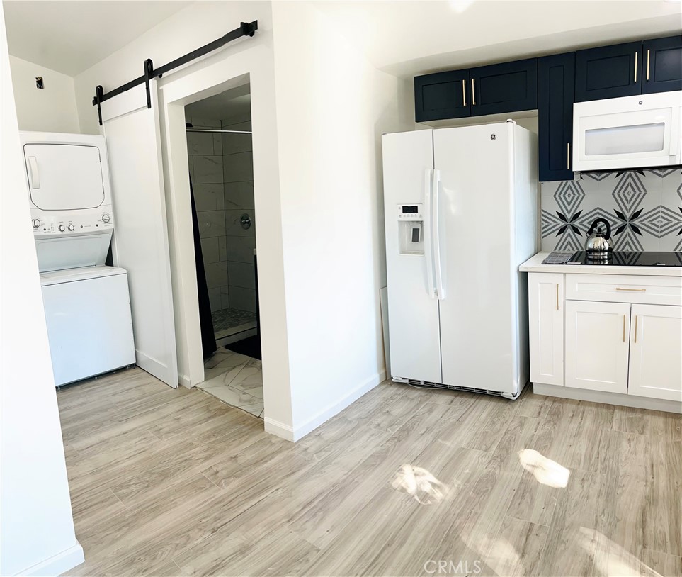 a view of a refrigerator in kitchen and an empty room with wooden floor