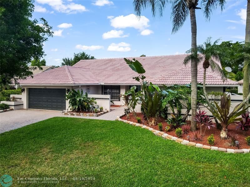 A beautifully paved driveway leads to an inviting front entrance, framed by lush, tropical landscaping and mature trees that provide both privacy and a touch of nature's tranquility.