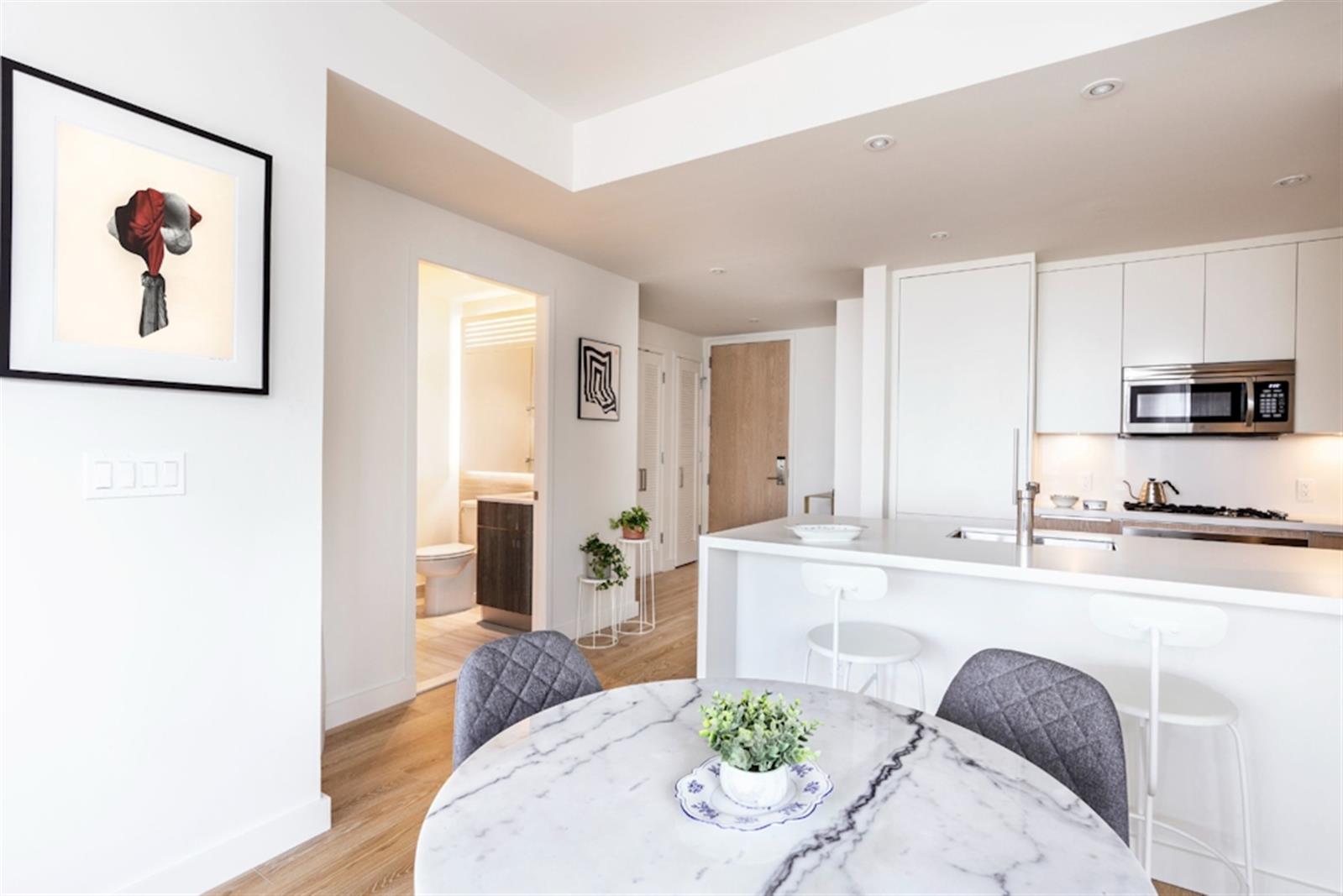 a living room with stainless steel appliances furniture wooden floor and a kitchen view