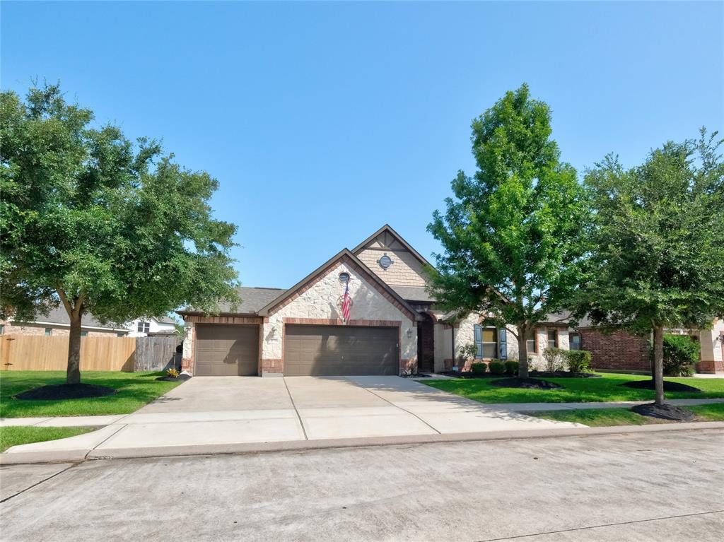 Welcome home to this is one-story home with a pretty brick and stone facade, a three car garage, and a well-maintained lawn, flanked by mature trees. The American flag adds a patriotic touch to the property's curb appeal.