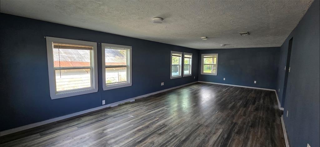 Spacious living area with dark wood flooring, blue walls, and ample natural light from multiple windows. Perfect for flexible living and entertaining.