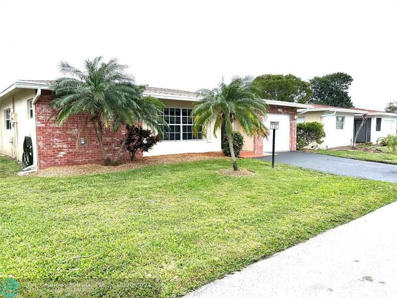 front view of house with a yard and palm trees