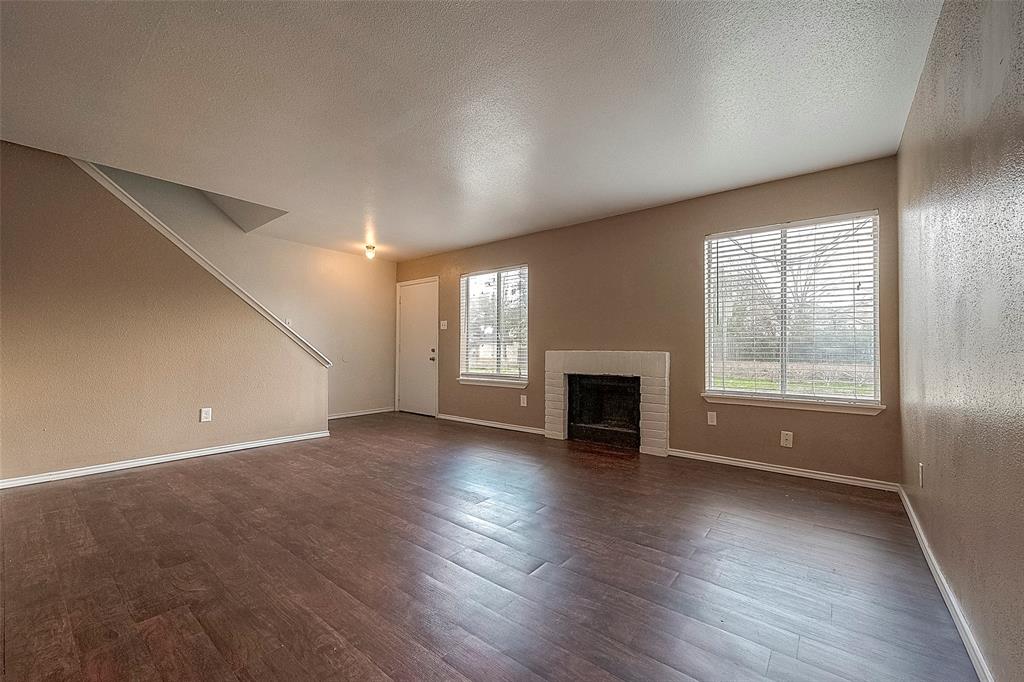 an empty room with wooden floor fireplace and windows