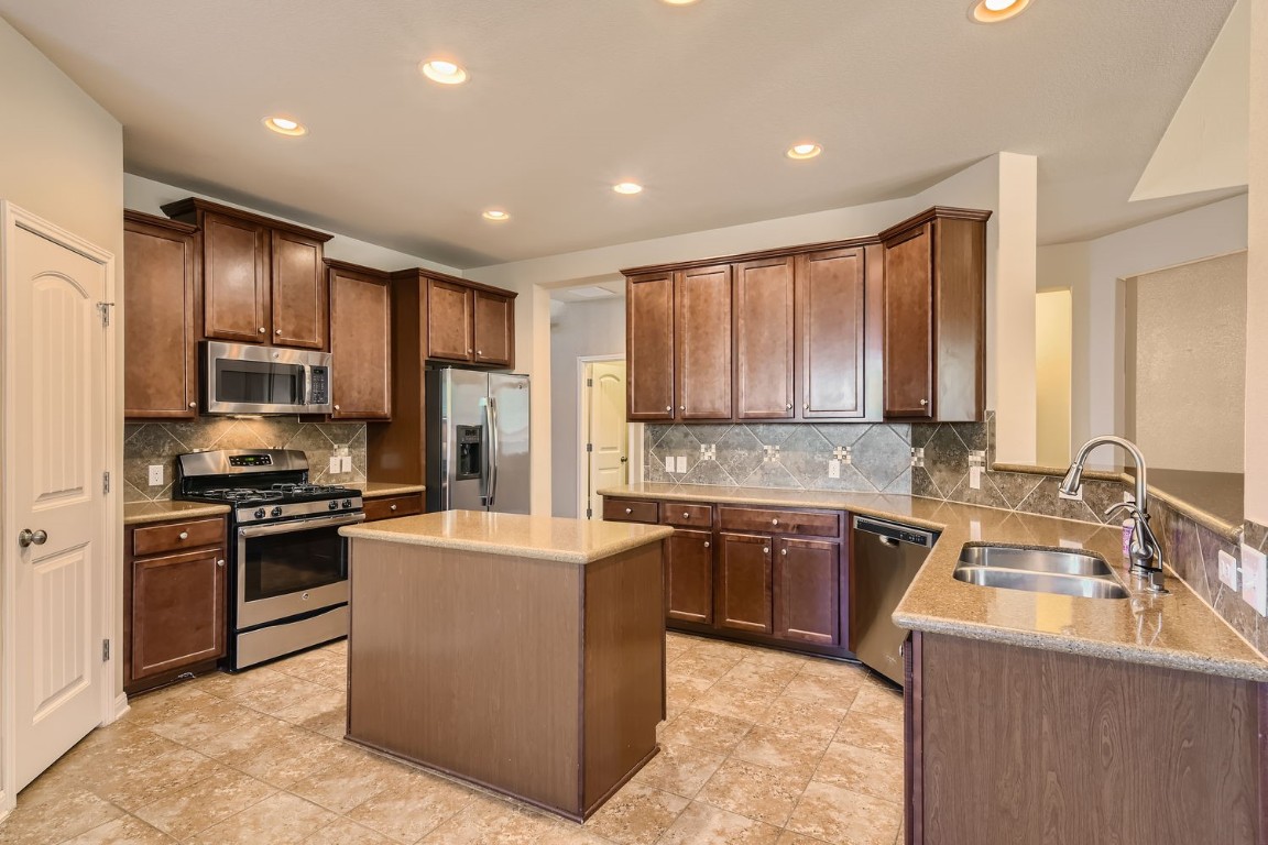 a kitchen with stainless steel appliances granite countertop a sink stove refrigerator and cabinets