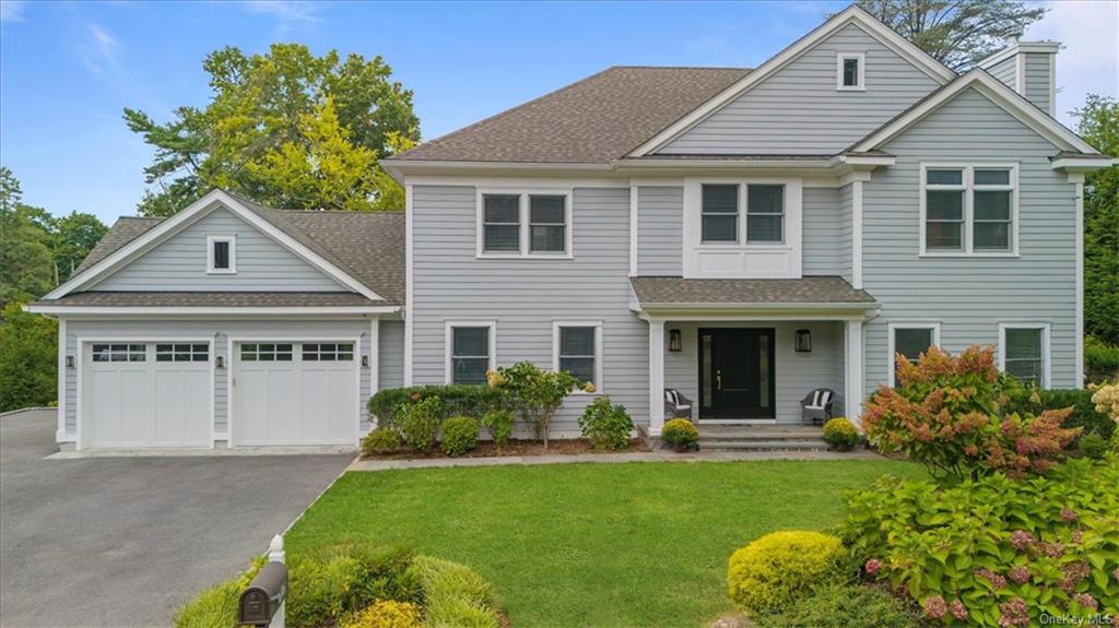 View of front facade with a garage, a front lawn and beautiful perennial plantings, and covered porch