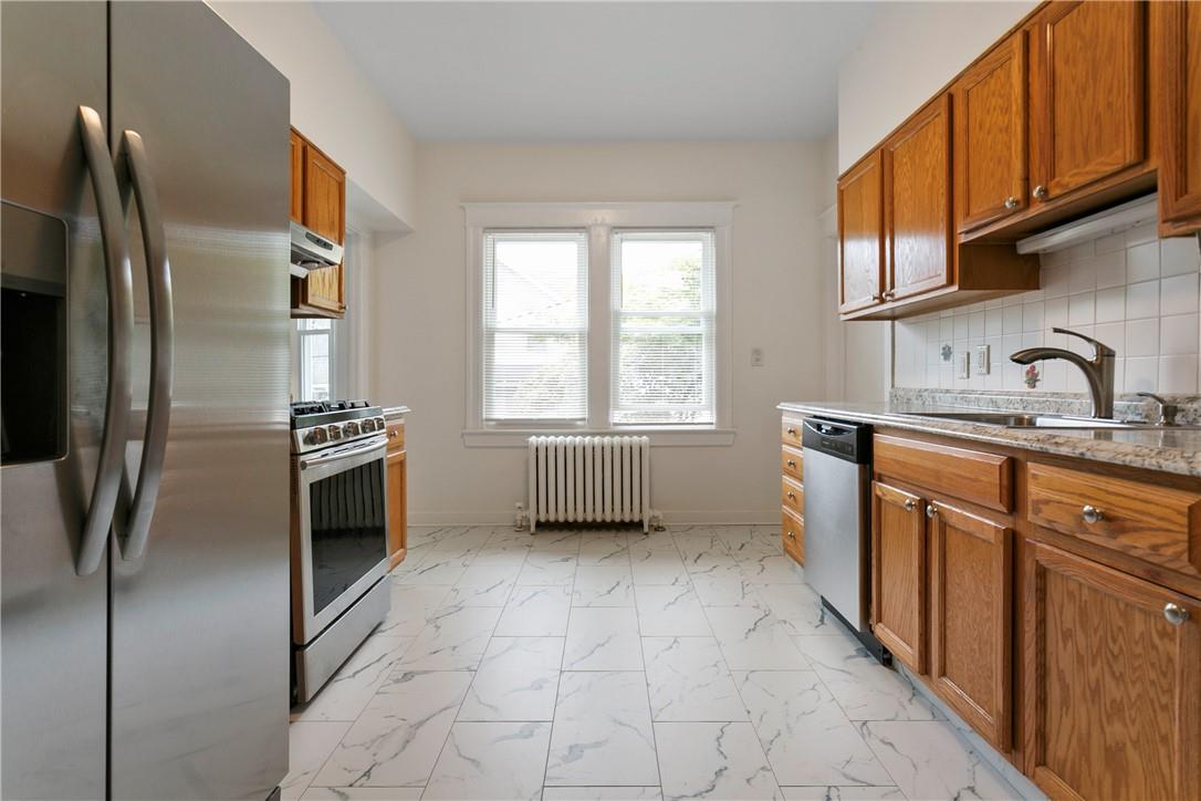 Kitchen with light stone counters, sink, decorative backsplash, appliances with stainless steel finishes, and radiator heating unit