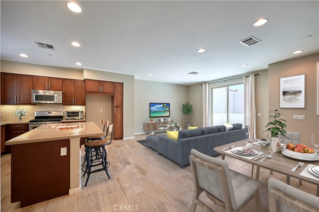 a kitchen with stainless steel appliances kitchen island granite countertop a refrigerator a stove top oven a dining table and chairs with wooden floor
