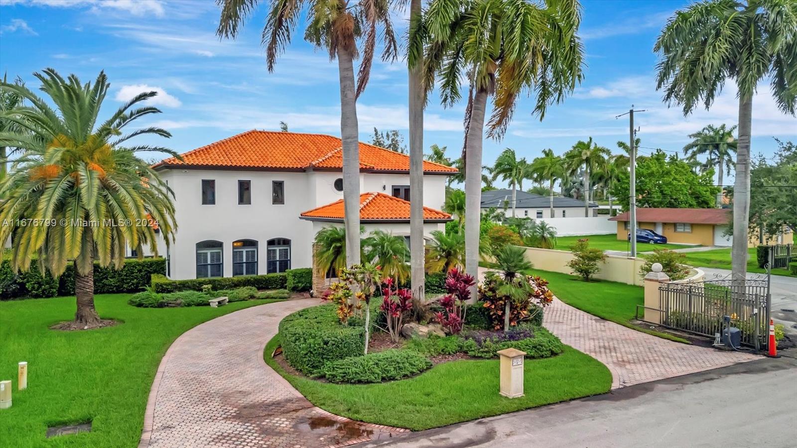 a view of a white house with a big yard potted plants and palm trees