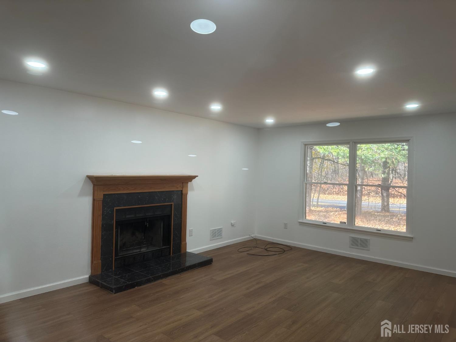 an empty room with wooden floor fireplace and windows