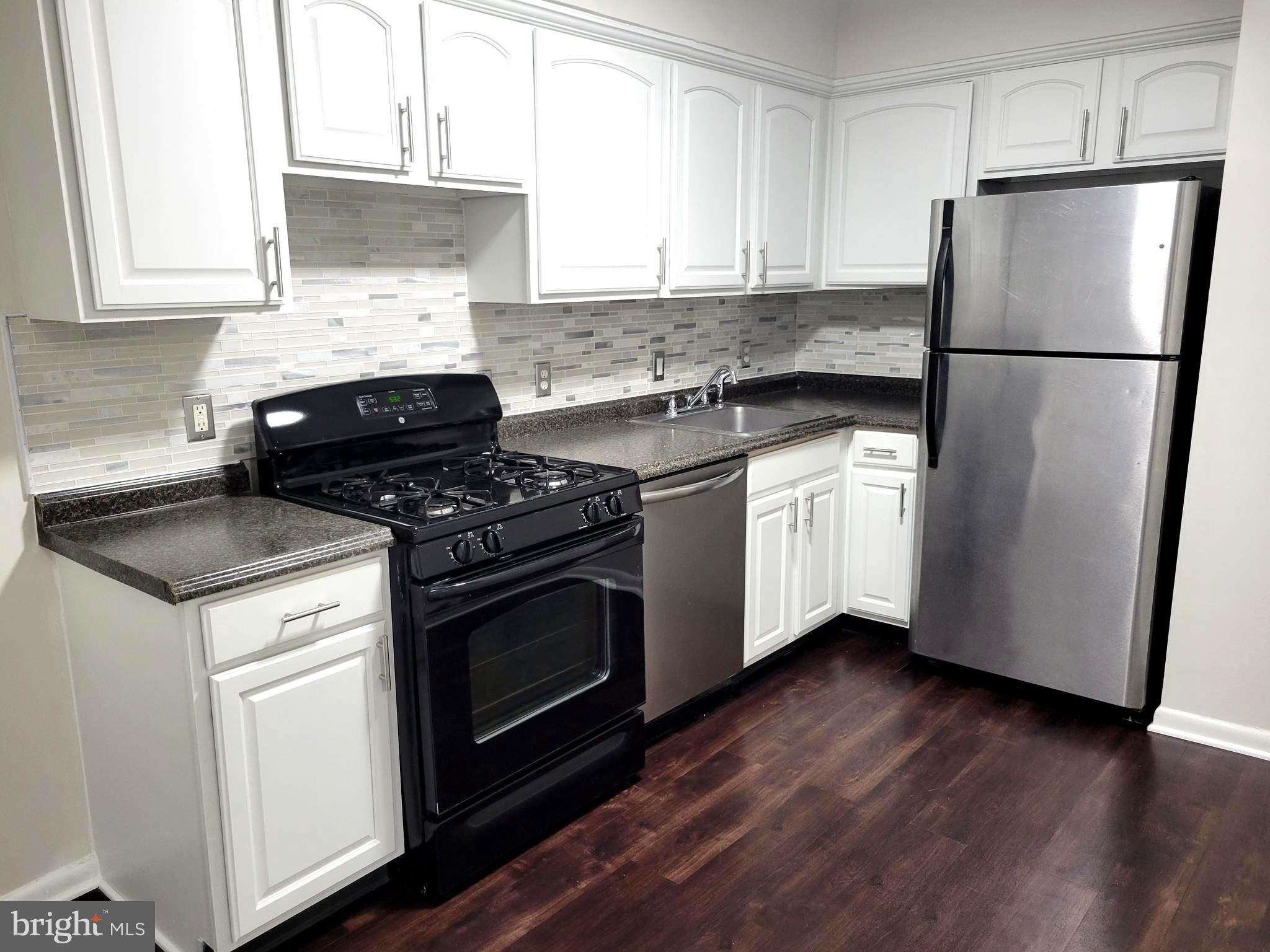 a kitchen with granite countertop wooden floors stainless steel appliances and white cabinets
