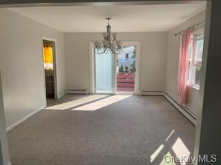 Carpeted empty room with baseboard heating and a chandelier