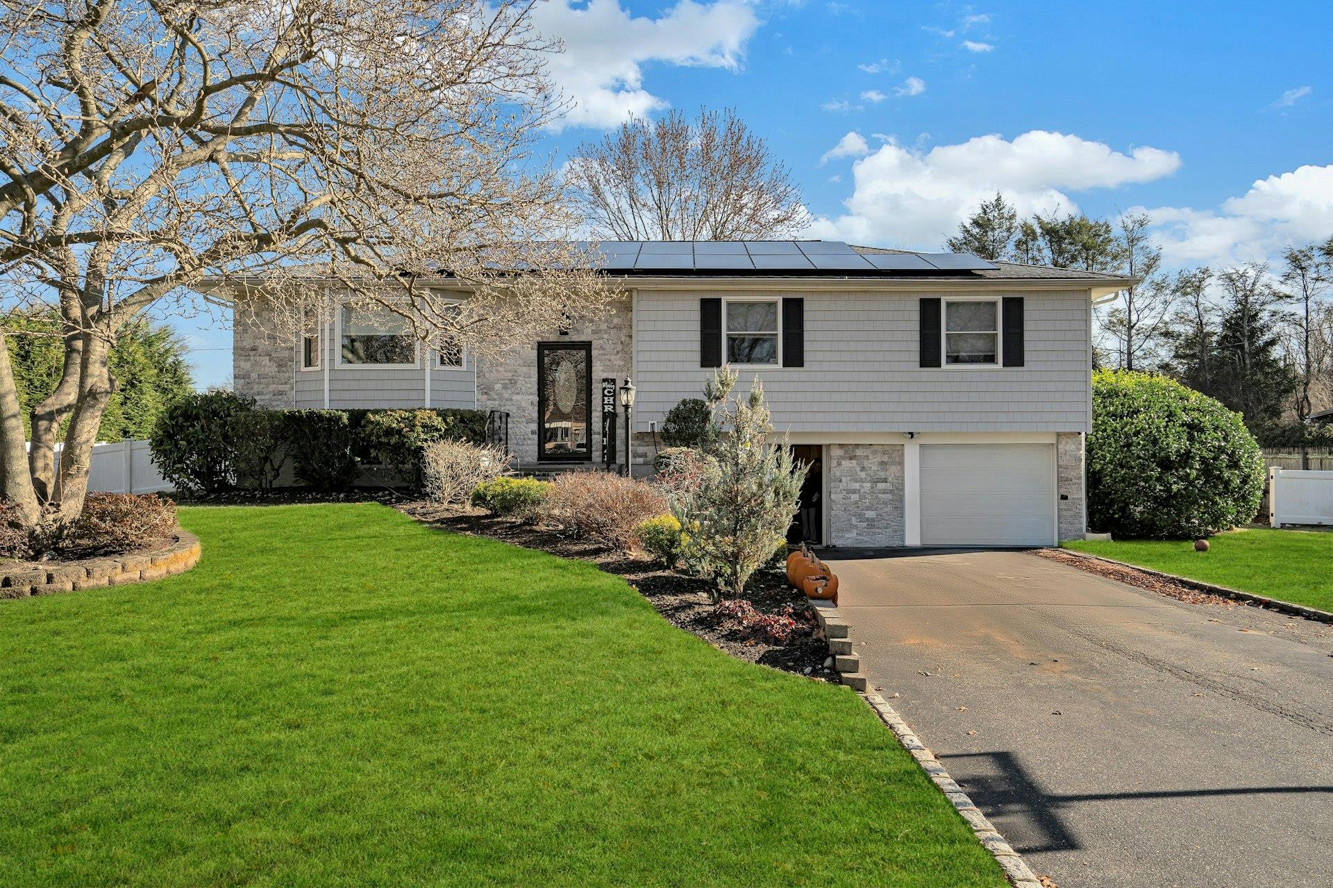 Split foyer home with solar panels, a garage, and a front lawn