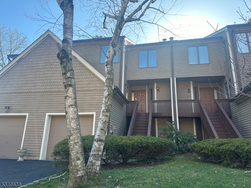 a view of a brick house with a yard plants and large tree