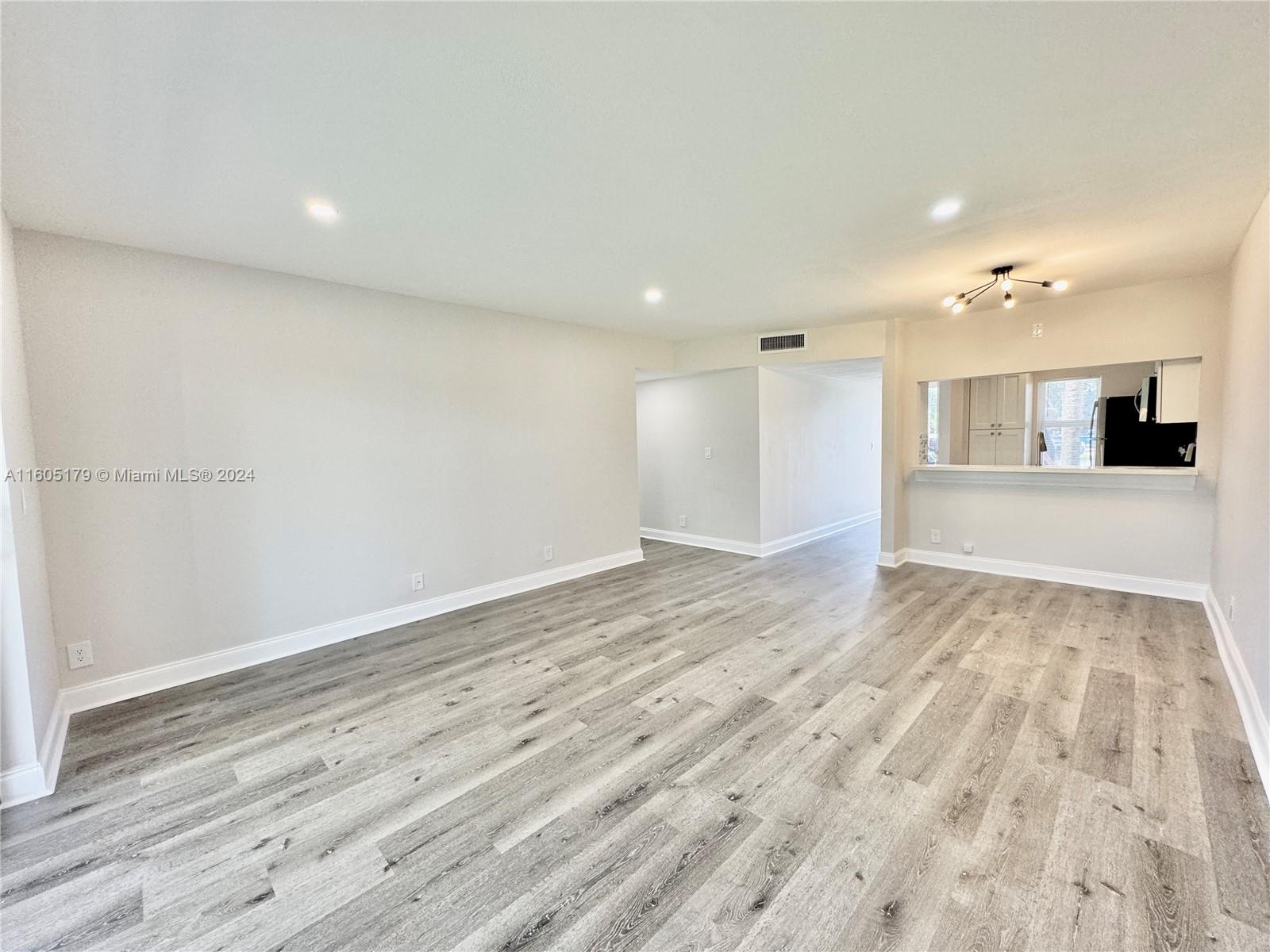 a view of an empty room with wooden floor and a kitchen