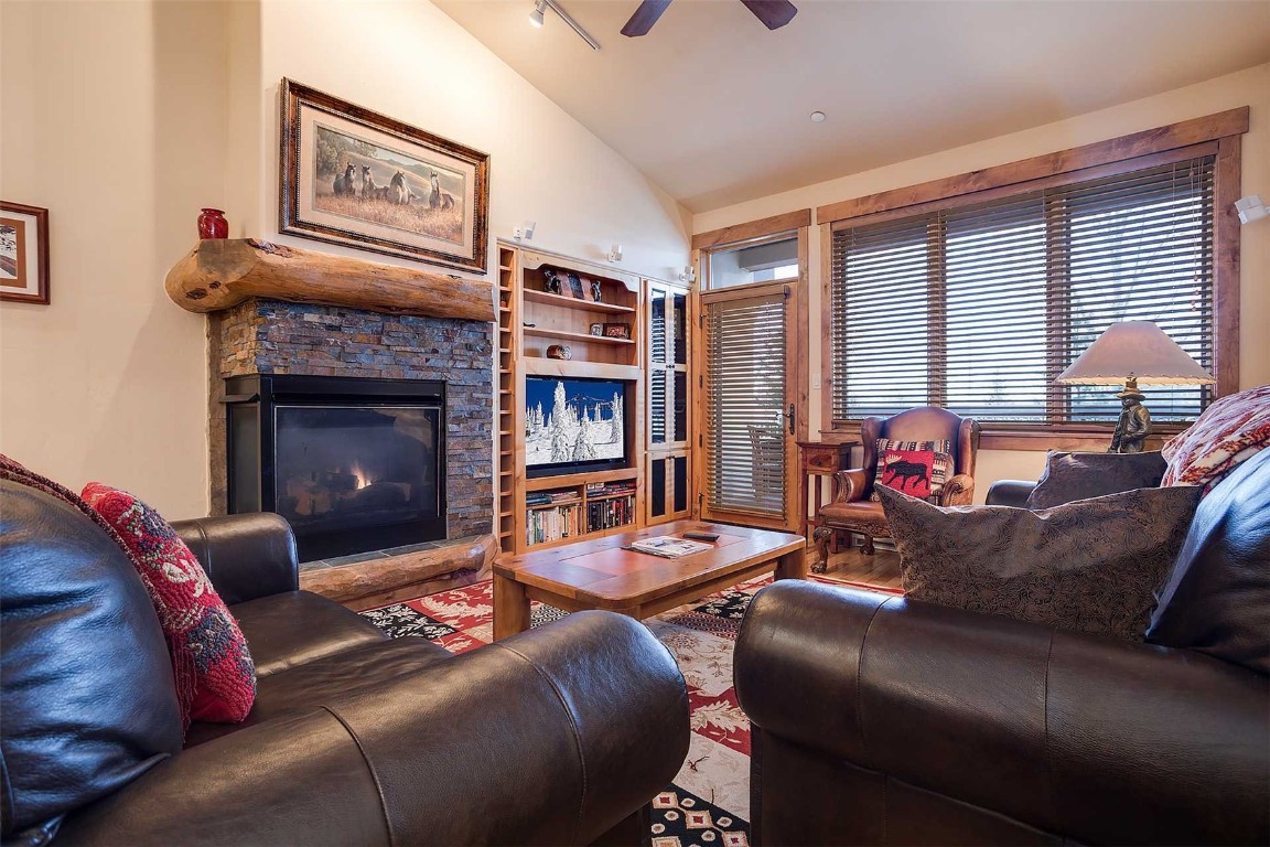 Living room with lofted ceiling, ceiling fan, and a stone fireplace