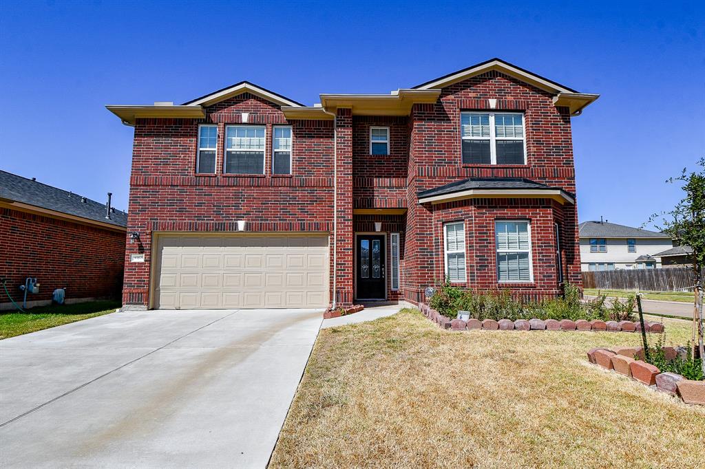 This is a two-story brick home with a two-car garage, featuring a well-maintained lawn and a neat front garden. The exterior has large windows and a welcoming entrance.