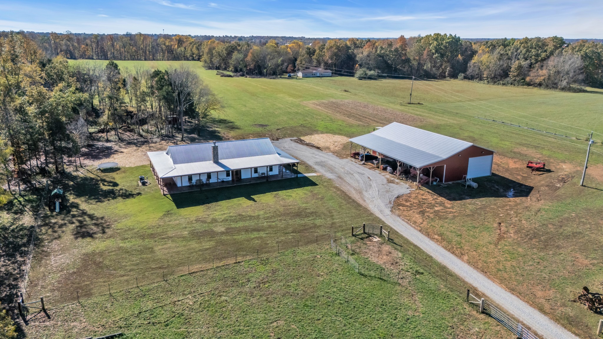 Aerial view of a 40-acre property in Springfield, TN featuring a modern farmhouse with rustic charm, surrounded by lush fields. Also with the property, a large 40x80 shop stands, offering ample space for work or storage.