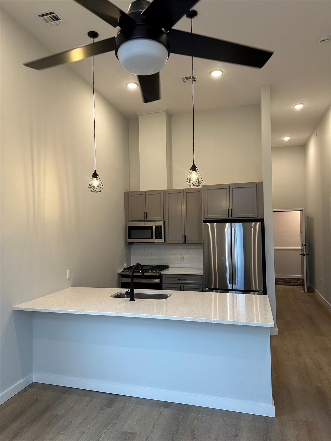 Kitchen with appliances with stainless steel finishes, backsplash, dark wood-type flooring, sink, and pendant lighting