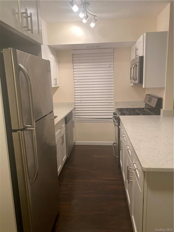 Kitchen with dark wood-type flooring, white cabinets, range, and fridge