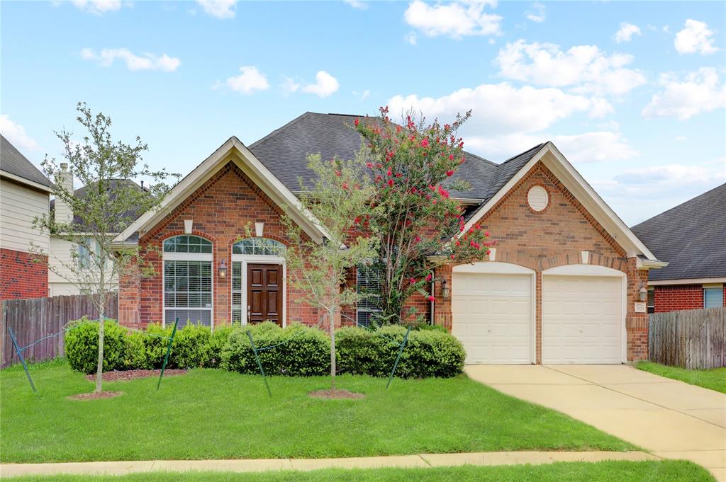 This is a single-story brick home featuring a double garage, arched windows, and a well-manicured lawn with mature landscaping.