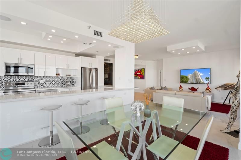 a view of kitchen with stainless steel appliances granite countertop dining table chairs sink and cabinets