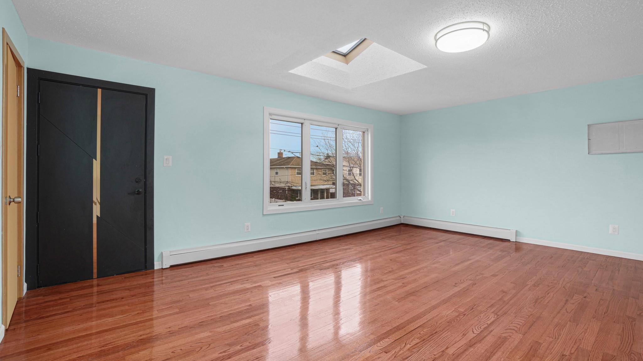 Unfurnished room with a skylight, a baseboard radiator, a textured ceiling, and light hardwood / wood-style floors