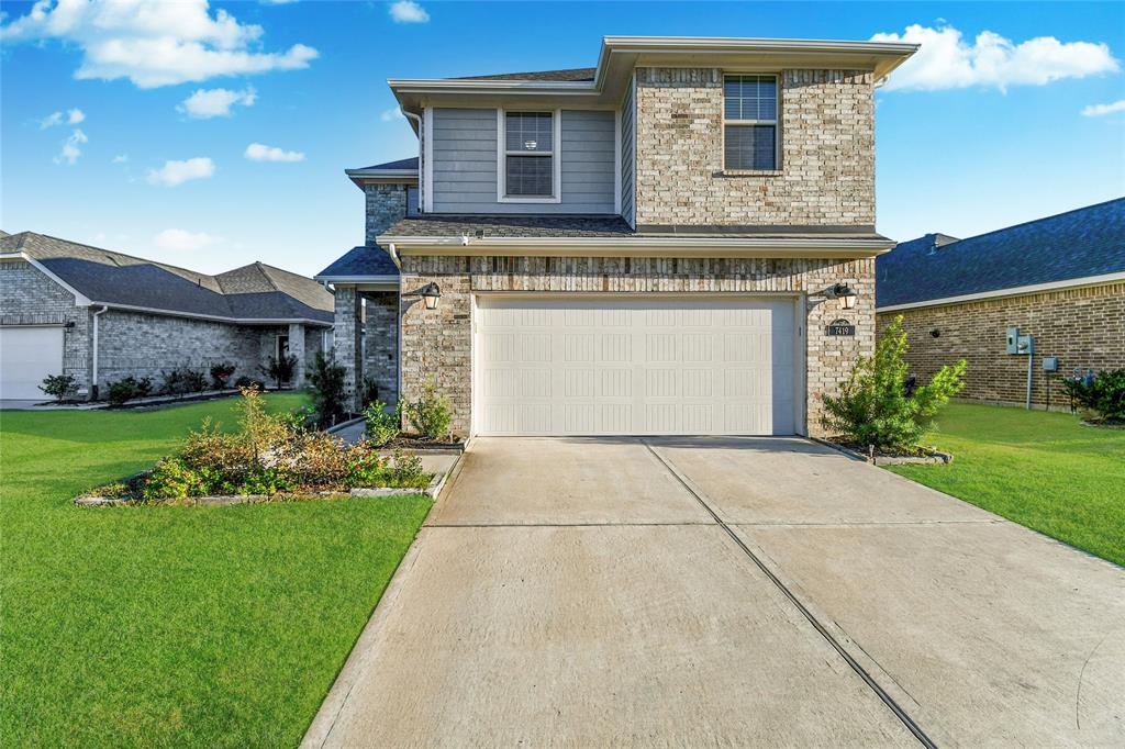 This is a two-story brick home with a two-car garage and a well-maintained driveway. It features a neatly landscaped front yard and a modern exterior design. From this view one can see the home is placed well on the property providing a spacious view.