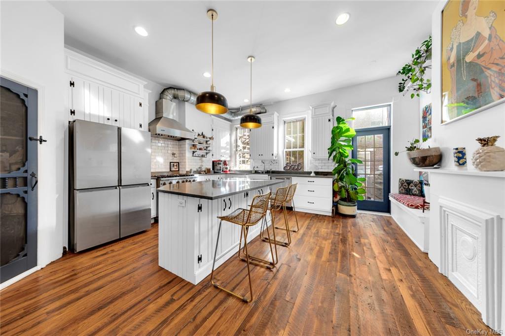 Kitchen with wall chimney range hood, stainless steel refrigerator, a kitchen island, and white cabinets