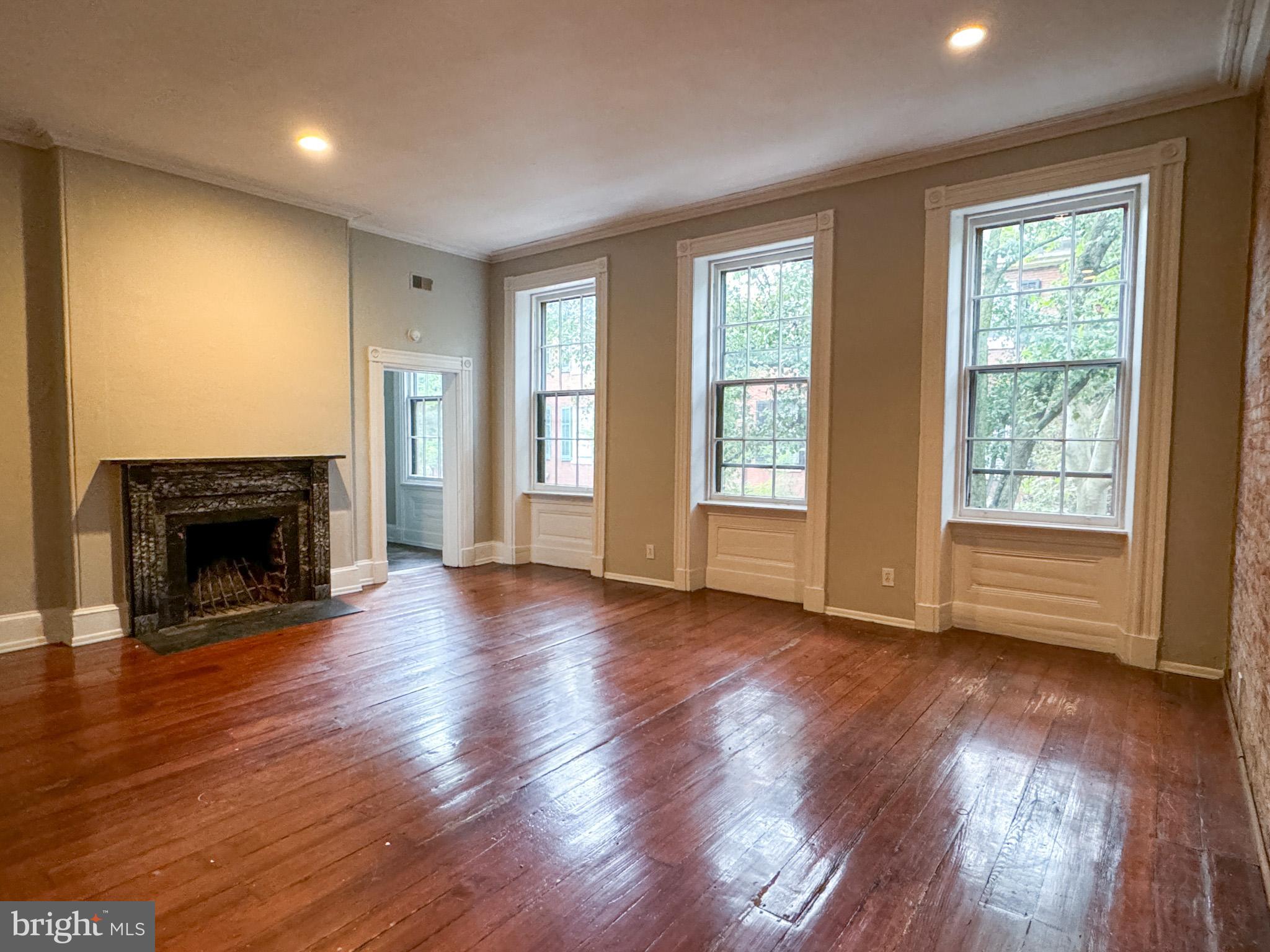 an empty room with wooden floor fireplace and windows