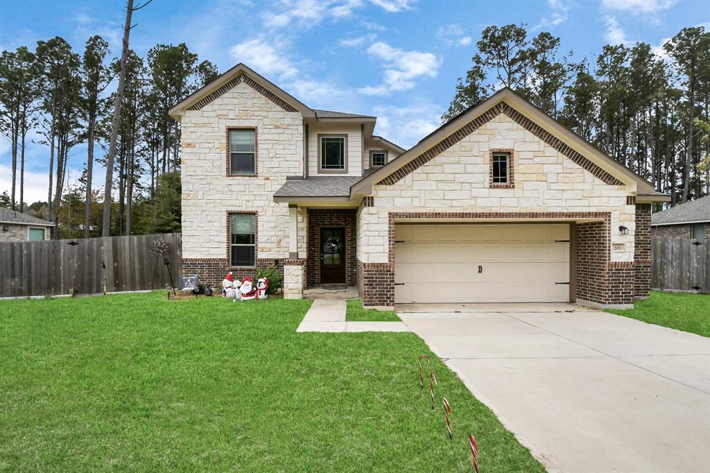 Charming two-story home with a stone and brick facade, featuring a spacious two-car garage and a well-maintained front lawn. The property is bordered by a wooden fence and surrounded by tall trees, offering both privacy and a scenic view.