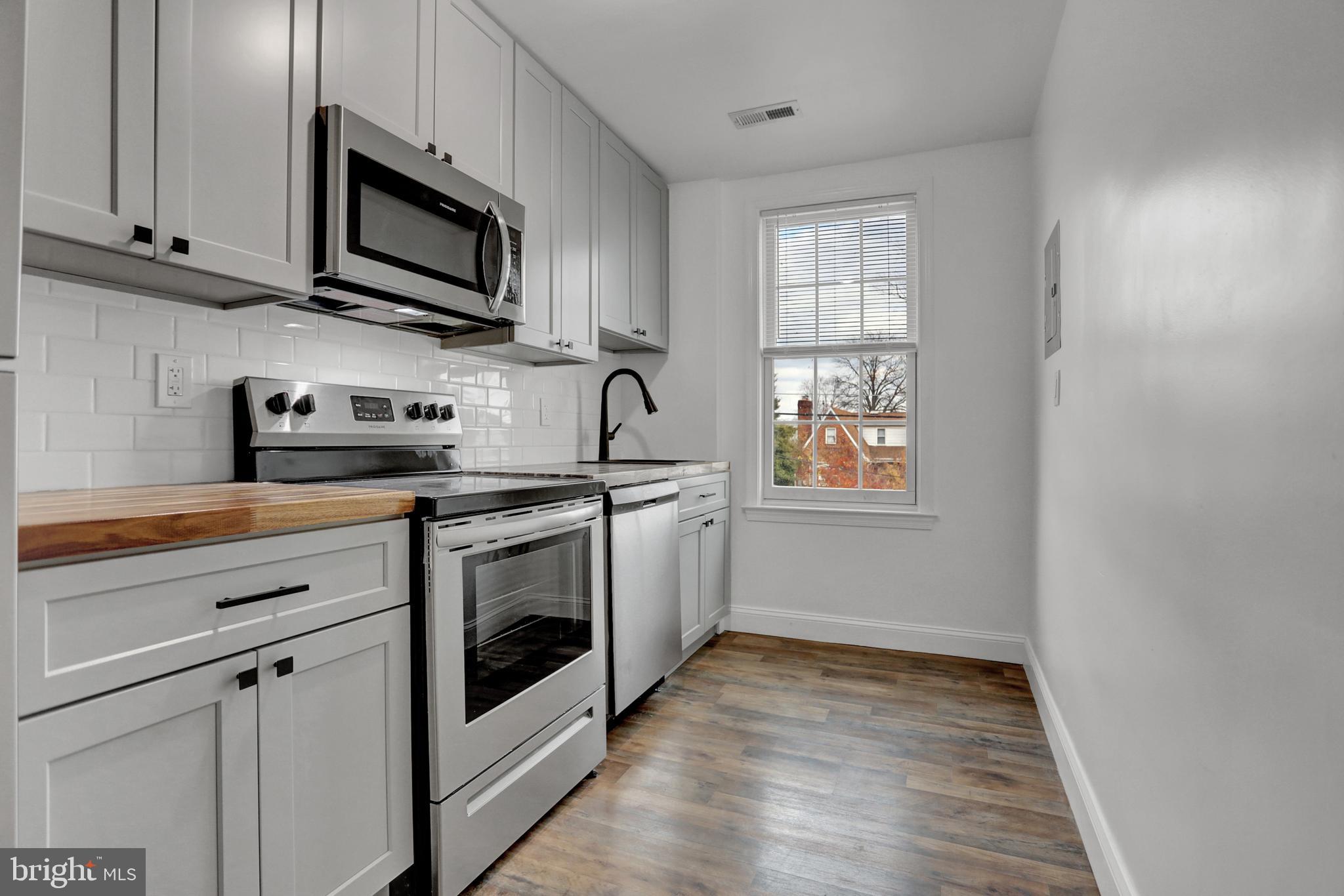 a kitchen with stainless steel appliances granite countertop white cabinets a sink a window and a wooden floor