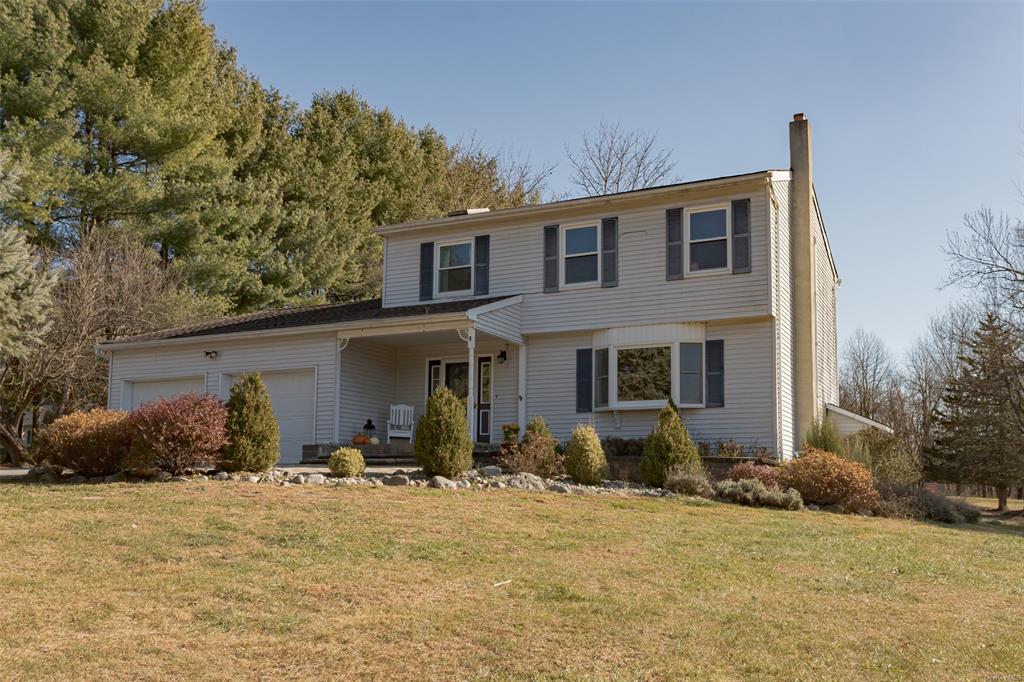 View of property featuring a porch, a garage, and a front lawn