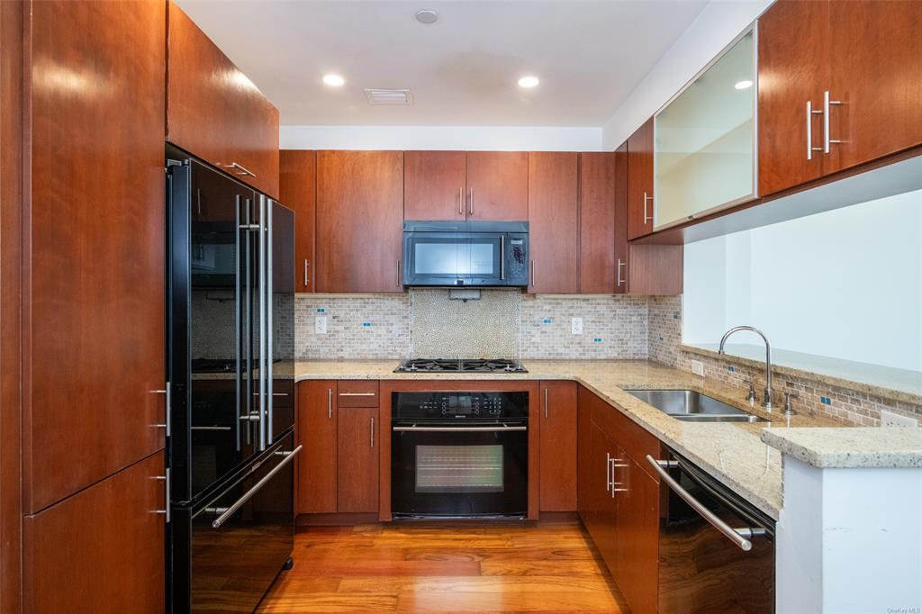 Kitchen featuring black appliances, sink, decorative backsplash, light wood-type flooring, and light stone counters