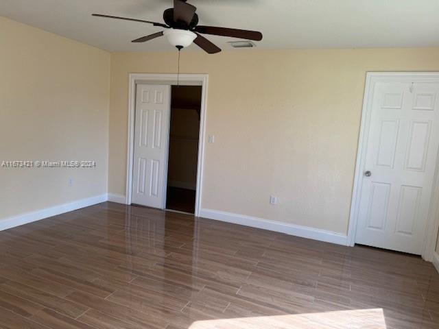 a view of an empty room with wooden floor and a ceiling fan