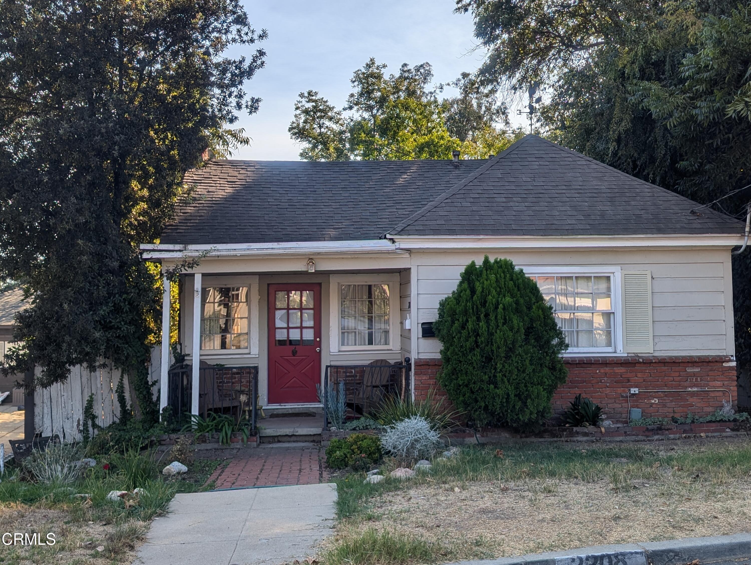 a view of a brick house with a large windows and a yard with plants and large trees