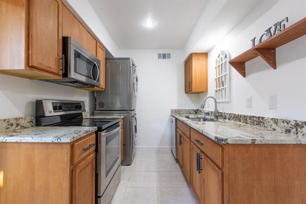 Kitchen featuring appliances with stainless steel finishes, sink, light tile patterned floors, and light stone counters