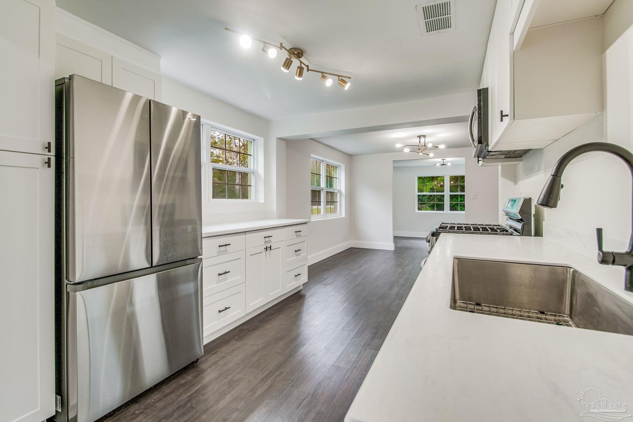 a kitchen with stainless steel appliances granite countertop a refrigerator a sink and a stove with wooden floors