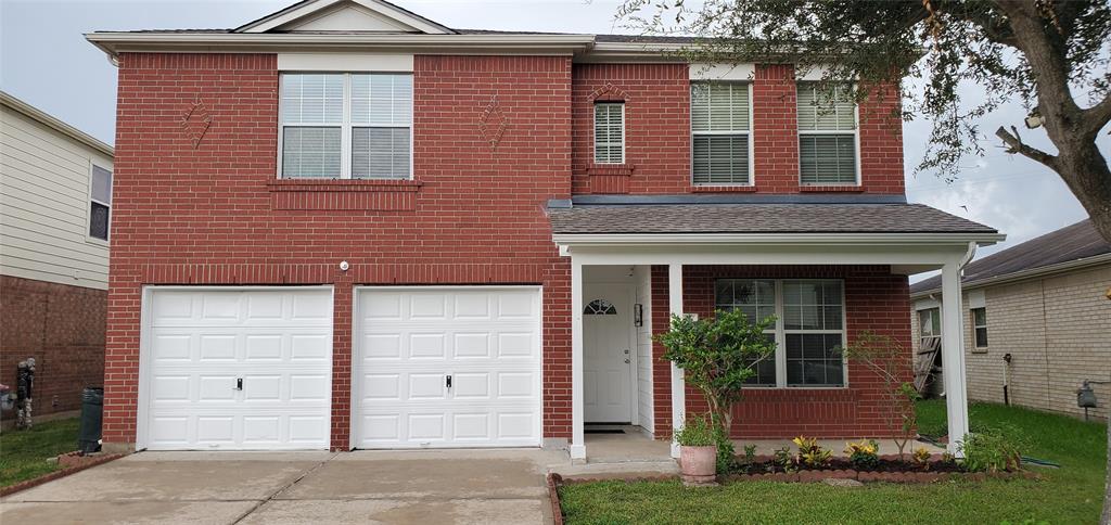 This is a two-story brick home featuring a double garage and a covered entryway, front porch,complemented by a  landscaped front yard.