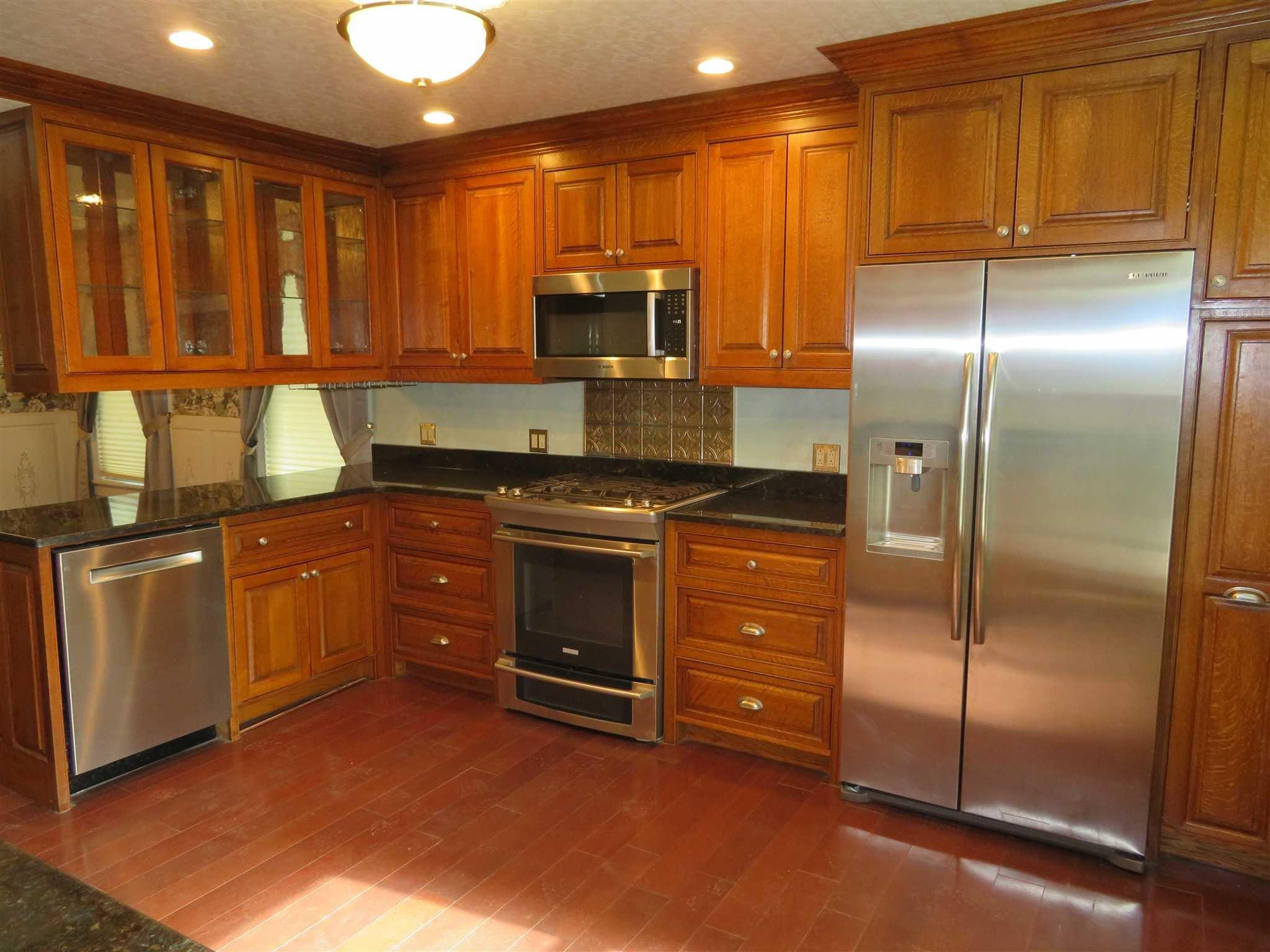 a kitchen with stainless steel appliances granite countertop a refrigerator a stove and a sink with wooden cabinets