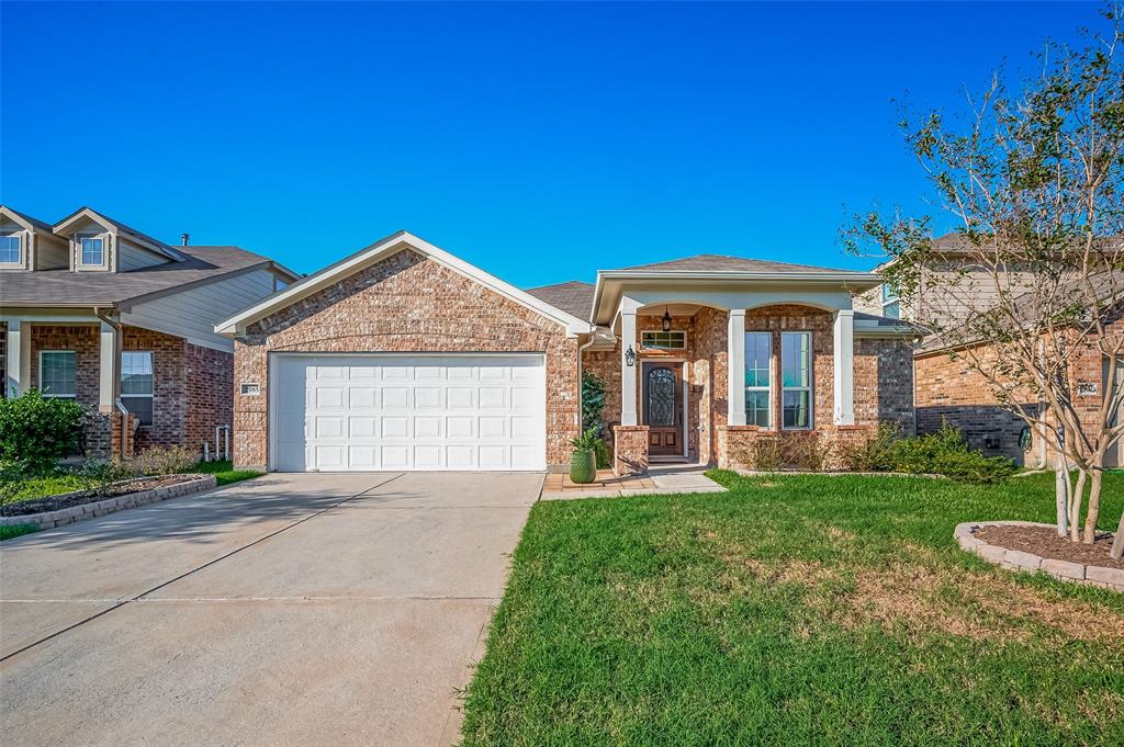 This is a single-story brick home featuring a two-car garage, arched entryway, and a well-manicured lawn. The neighborhood appears to be a tidy, residential area.