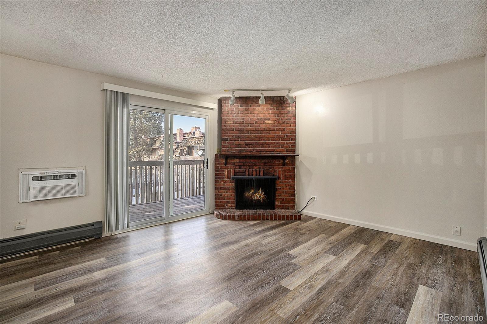 a view of an empty room with wooden floor fireplace and a window